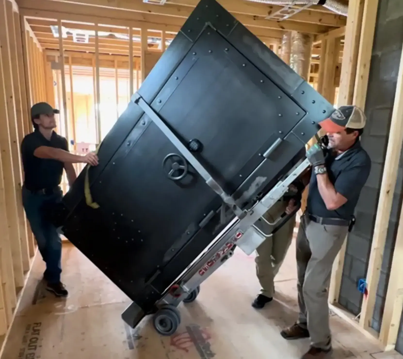 Three men moving a large black cabinet on a dolly.