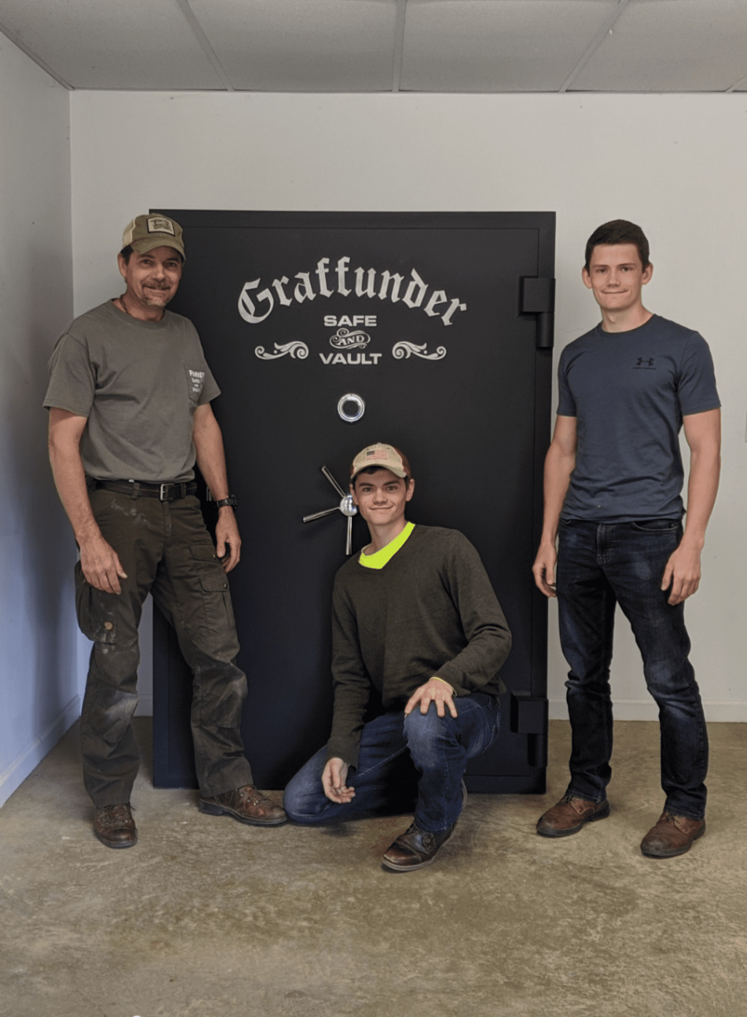 Three men are posing in front of a large safe.